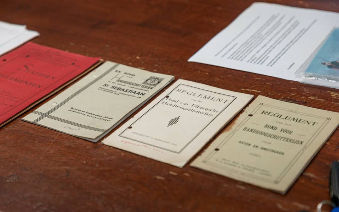 Op een houten tafel liggen diverse historische boekjes en documenten waarin de kunst van het handboogschieten wordt beschreven.