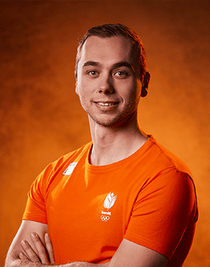 Een man in een oranje shirt met een Olympisch logo, dat doet denken aan iemand die uitblinkt in de handboogsport, staat met zijn armen over elkaar tegen een oranje verloopachtergrond.